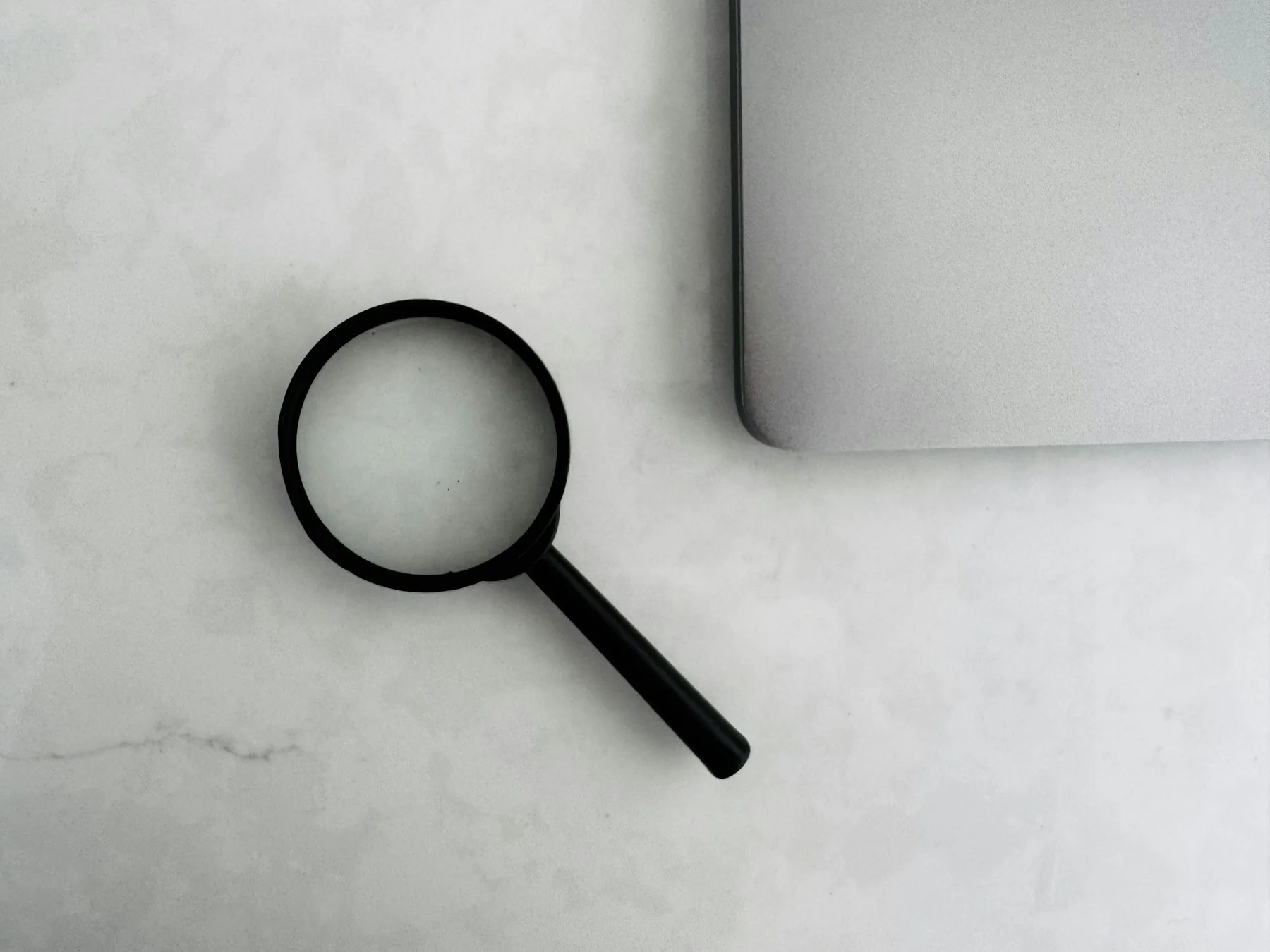 Magnifying glass resting beside a closed laptop on a white marble desk, symbolizing AI-powered search and online research Magnifying glass resting beside a closed laptop on a white marble desk, symbolizing AI-powered search and online research