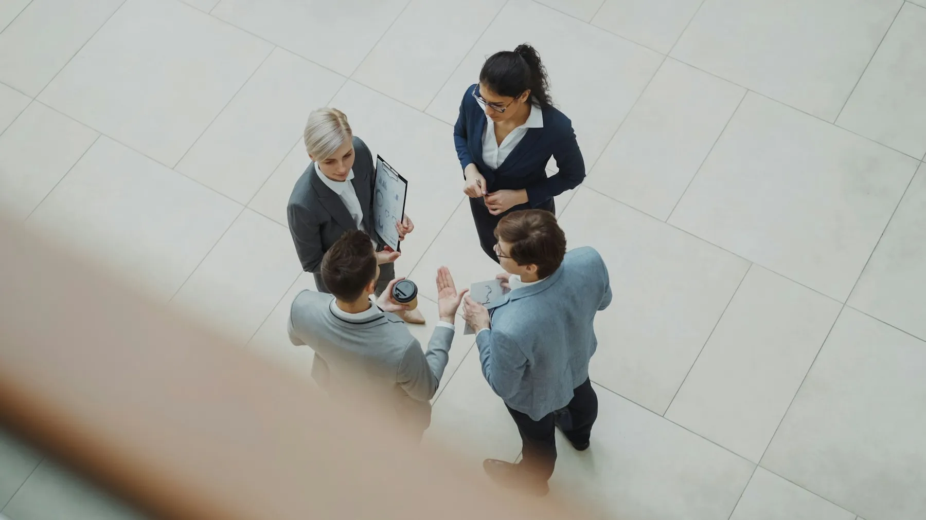 Four business professionals discussing financial charts together in a modern office lobby Four business professionals discussing financial charts together in a modern office lobby
