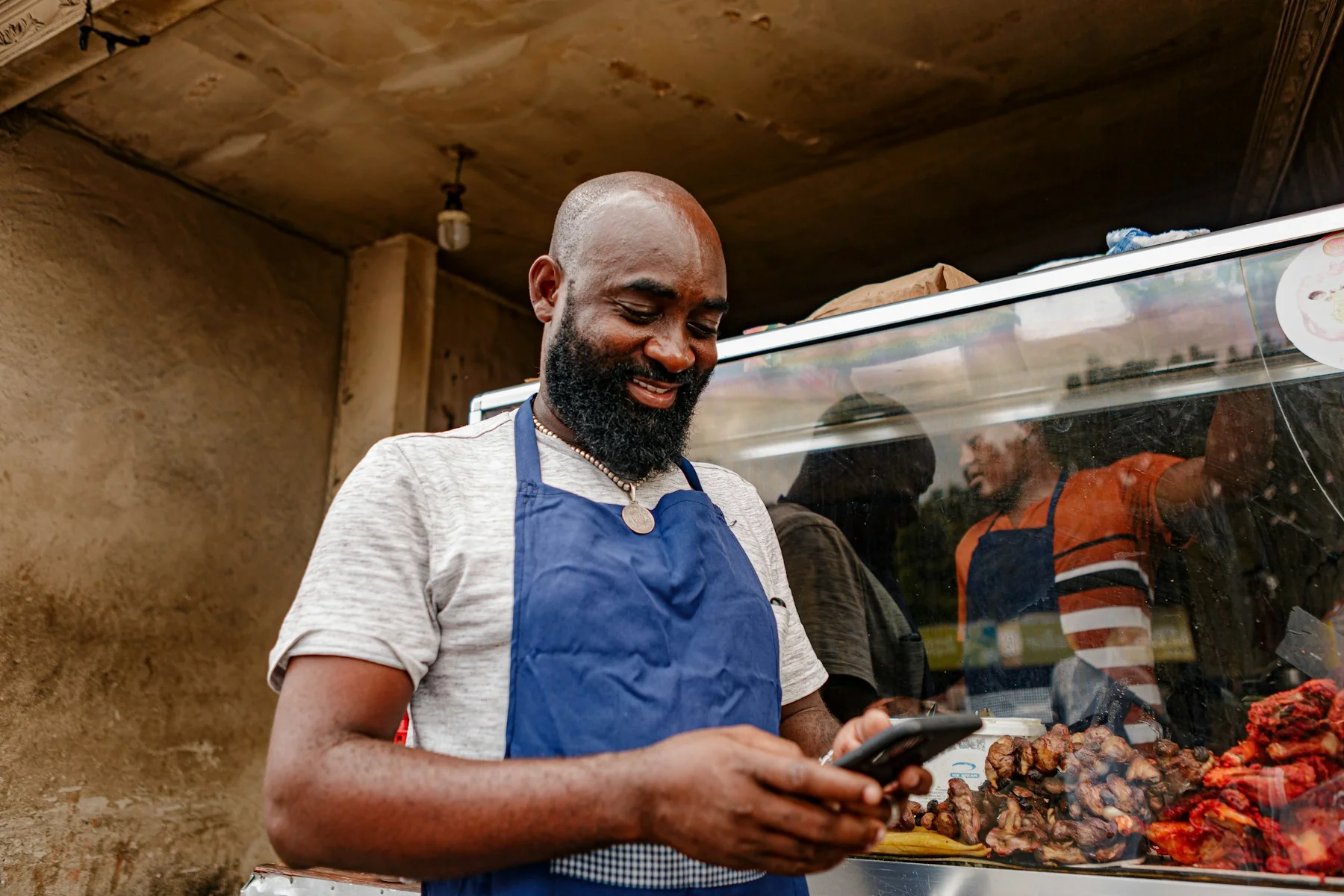 Smiling small business owner in an apron checking his phone at his food stall counter