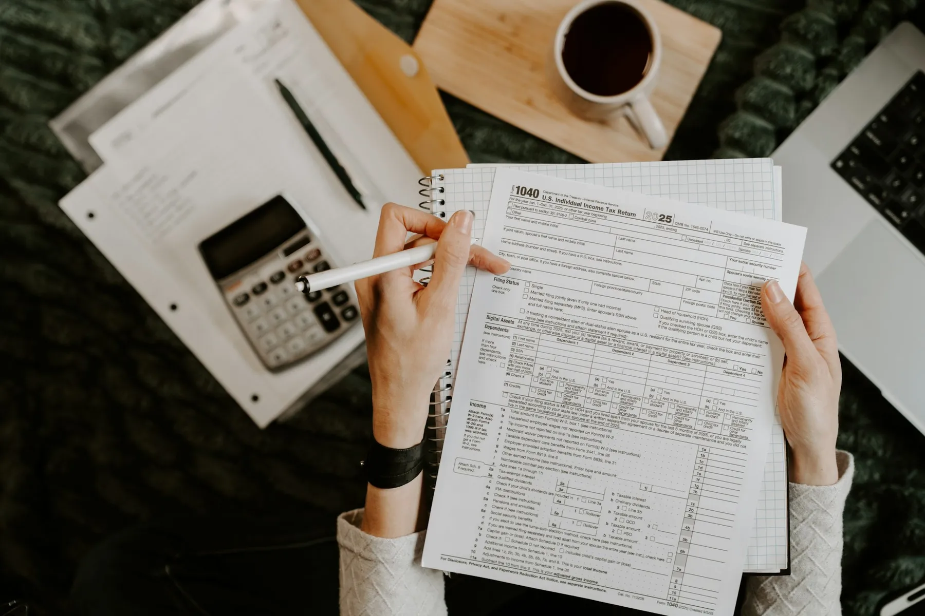 Person reviewing financial documents with a calculator and laptop on a clean desk